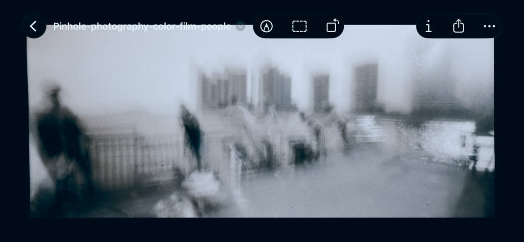 After Bleach Bypass Effect is applied in Photoshop - A blurry black and white photograph showing an outdoor urban scene with indistinct figures, railings, and buildings, framed by a dark interface border.
