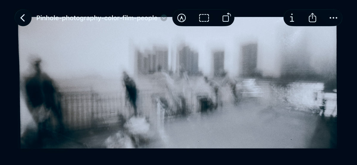 After Bleach Bypass Effect is applied in Photoshop - A blurry black and white photograph showing an outdoor urban scene with indistinct figures, railings, and buildings, framed by a dark interface border.